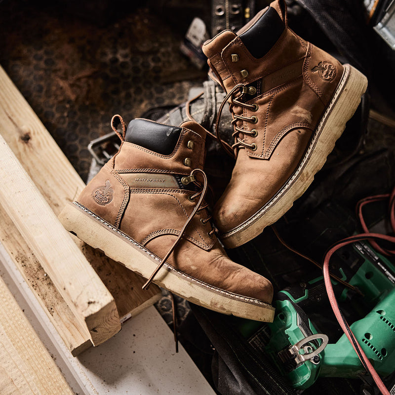 Pair of brown work boots on a construction site with tools and materials.