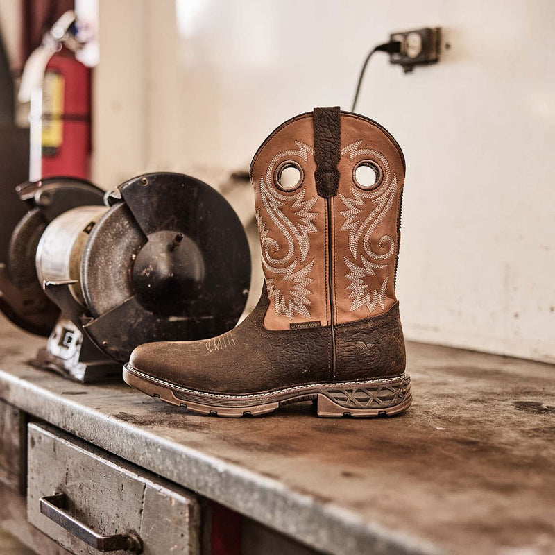 Brown cowboy boot with intricate design on a wooden surface in a workshop setting.