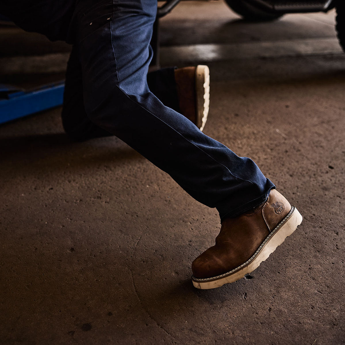 Person wearing brown boots and blue jeans on a concrete floor.