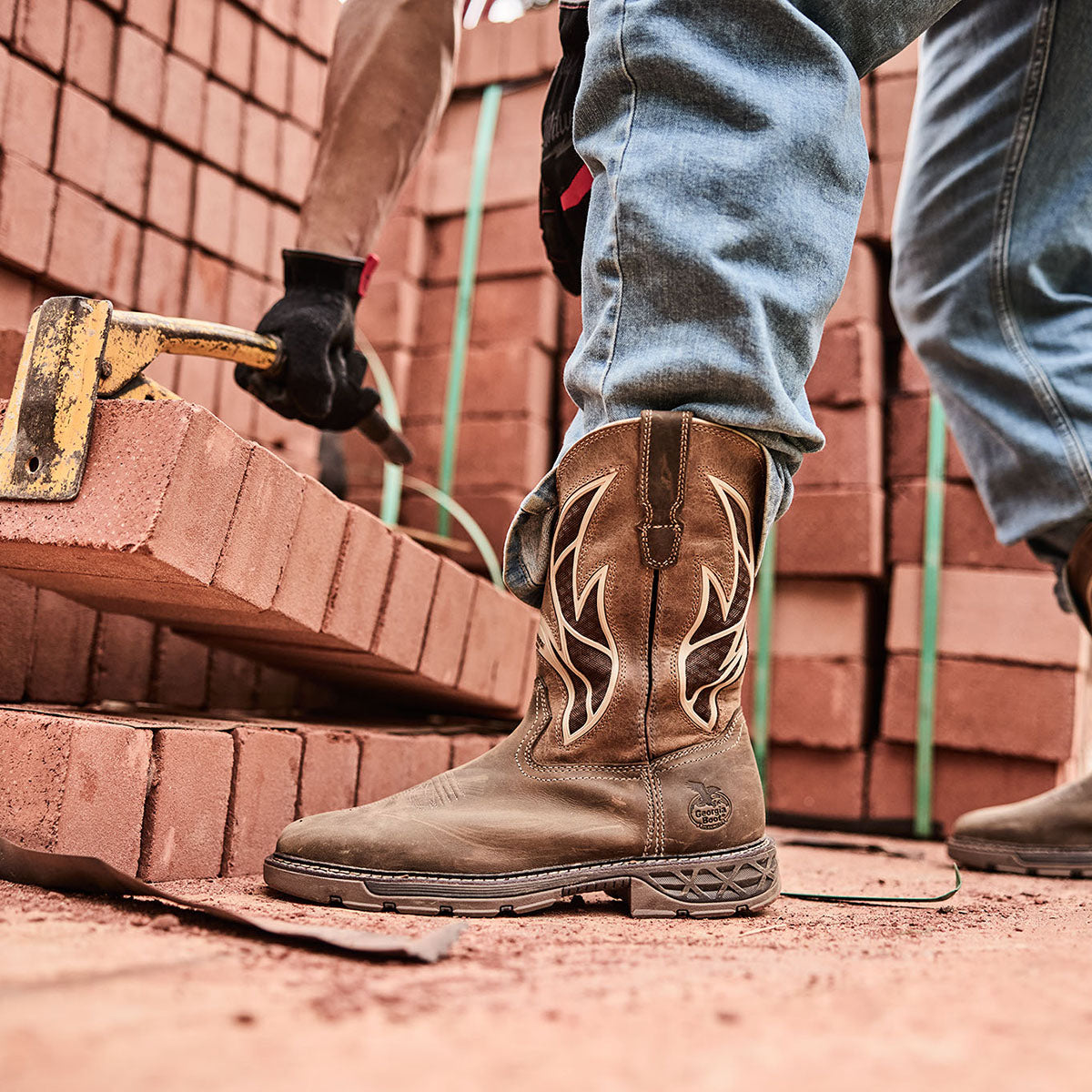 Brown work boot with decorative pattern worn by a person working with bricks.